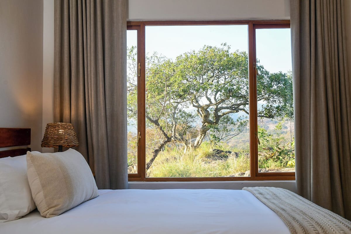 A bedroom with a large window, a bed, and a lamp.