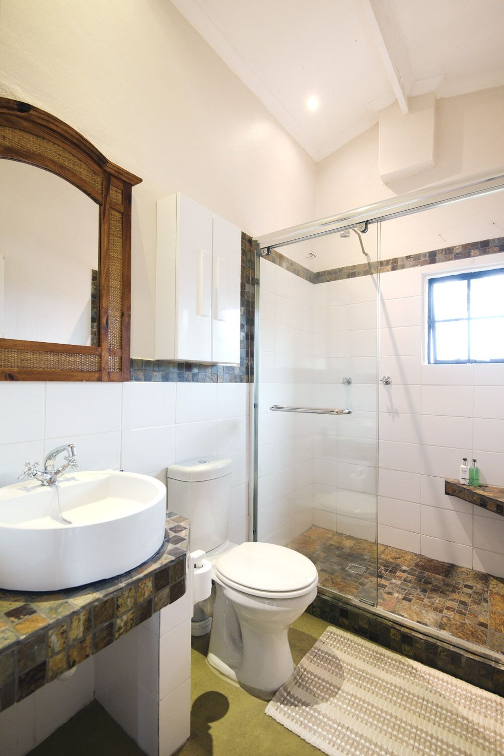 Une salle de bain avec un lavabo blanc, des toilettes, une douche à parois de verre et un miroir au-dessus du lavabo.
