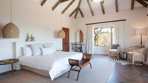 A bedroom with a large bed, wooden chairs, a desk, and a window with curtains. - Tomjachu Bush Retreat (Mbombela)