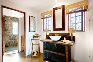 A bathroom with a stone wall, a wooden ladder, a large mirror, and a sink with a wooden countertop. - Tomjachu Bush Retreat (Mbombela)