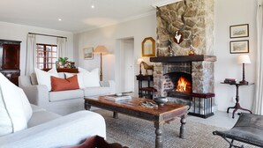 A cozy living room with a stone fireplace, a sofa, a coffee table, and a bookshelf. - Tomjachu Bush Retreat (Mbombela)