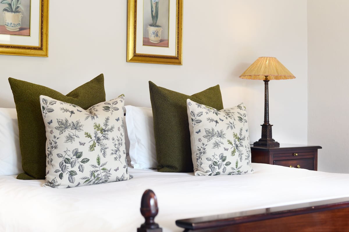 A neatly made bed with floral pillows, a lamp, and two framed pictures on the wall.