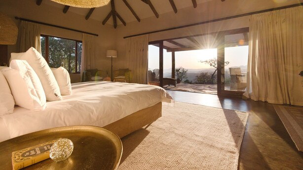 A spacious bedroom with a large bed, a view of the outdoors, and a rustic ceiling. - Tomjachu Bush Retreat (Mbombela)