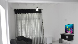 A modern living room with a black leather sofa, a white TV stand, and a large window with sheer curtains. - City Resort (Anuradhapura)