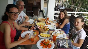 A family dining at an outdoor table with various dishes, drinks, and a book. - City Resort (Anuradhapura)