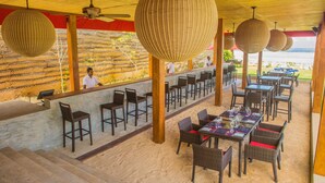 An outdoor dining area with wicker furniture, a bar, and a view of the ocean.
