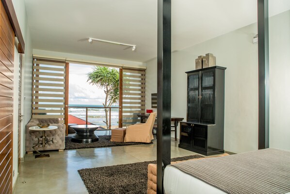 Un dormitorio moderno con una cama grande, un mueble para televisión y una zona de estar con vista al océano.
