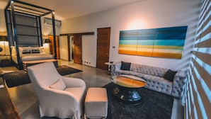 A modern living room with a white armchair, a tufted sofa, and a coffee table. There is a painting of a beach scene on the wall.