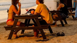 A beachside picnic area with wooden tables and benches, overlooking the sea.