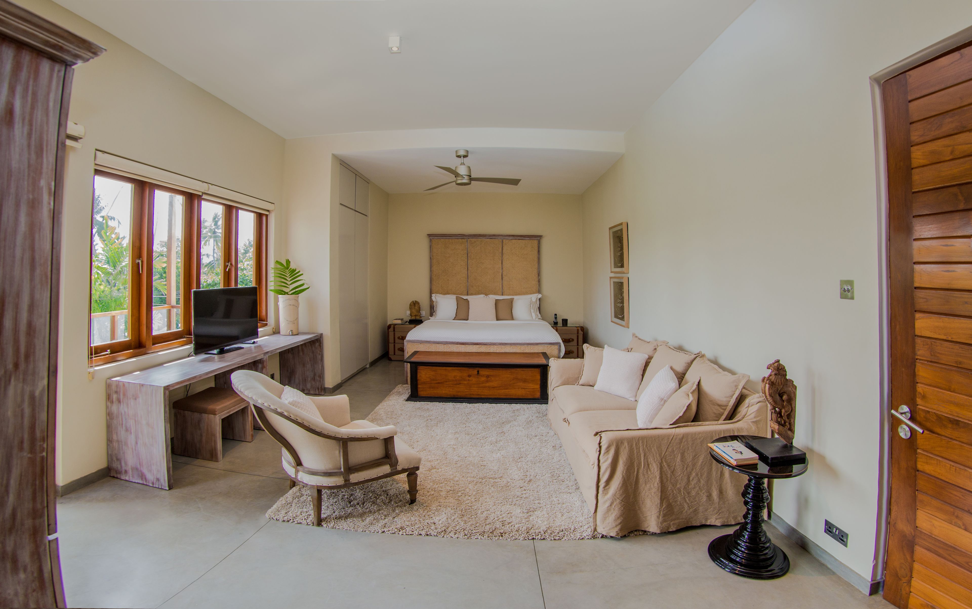 A bedroom with a bed, a desk, a chair, a TV, and a ceiling fan.