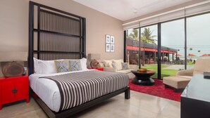 A modern bedroom with a large bed, a red nightstand, a black-framed bookshelf, and a large window offering a view of the outdoors.