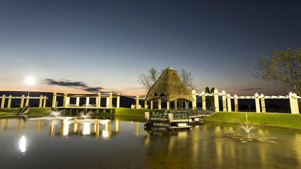 A tranquil lakeside setting with a thatched-roof pavilion, a fountain, and a well-maintained lawn.