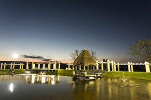 Um ambiente tranquilo à beira do lago com um pavilhão de colmo, uma fonte e um gramado bem cuidado.