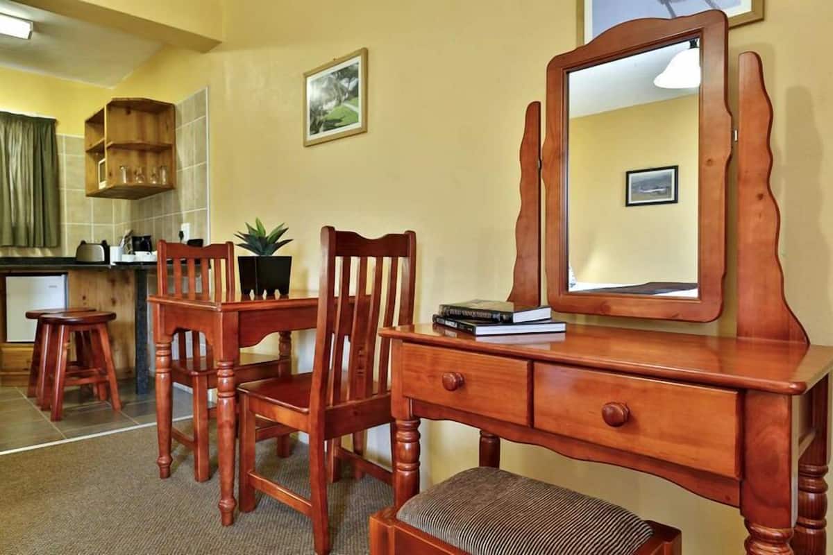 A wooden dresser with a mirror, a chair, and a small table in a room with a tiled backsplash and a picture on the wall.