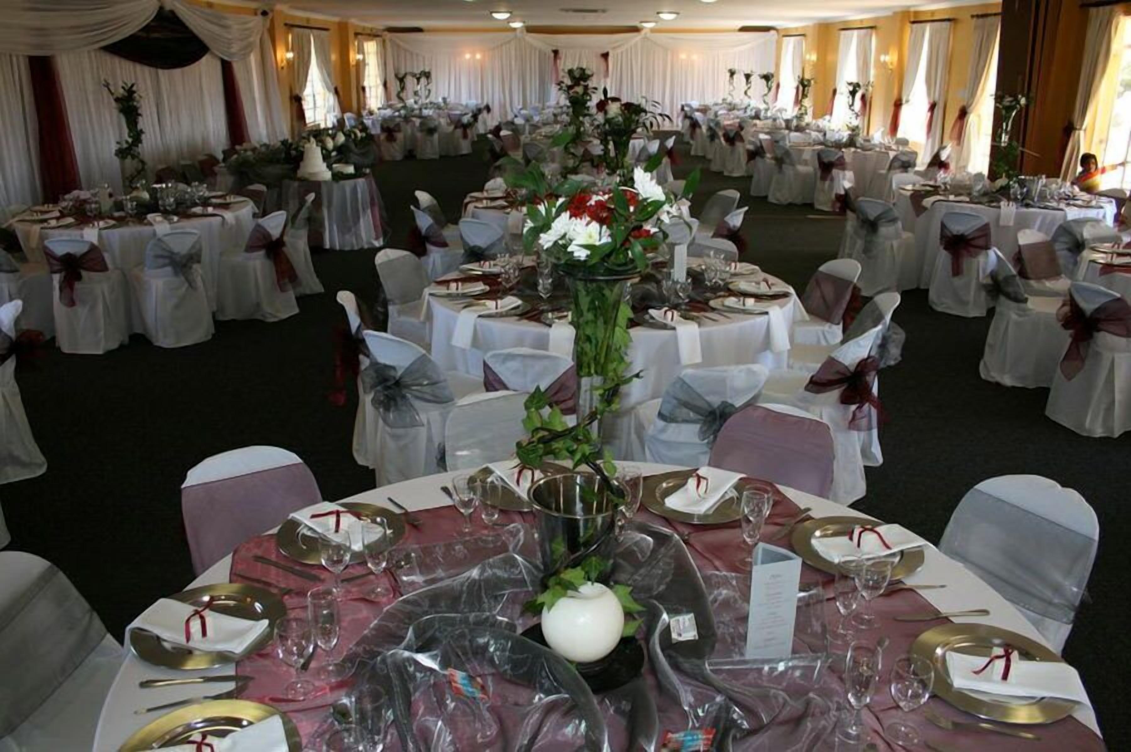 Ein Festsaal mit runden Tischen, festlich gedeckt für eine formelle Veranstaltung, mit weißen Tischdecken, gold- und weißem Besteck und floralen Tischarrangements.