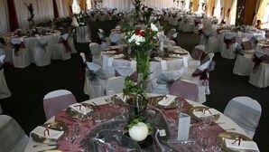 A banquet hall with round tables set for a formal event, featuring white tablecloths, gold and white cutlery, and floral centerpieces.