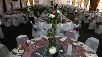 Ein Festsaal mit runden Tischen, festlich gedeckt für eine formelle Veranstaltung, mit weißen Tischdecken, gold- und weißem Besteck und floralen Tischarrangements.