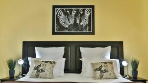 A neatly made bed with white linens and two decorative pillows, a dark headboard, and a framed artwork above.