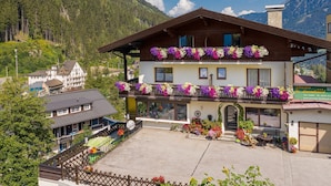 A two-story building with balconies adorned with colorful flowers, a paved courtyard, and a mountainous backdrop. - Pension St. Leonhard (Bad Gastein)