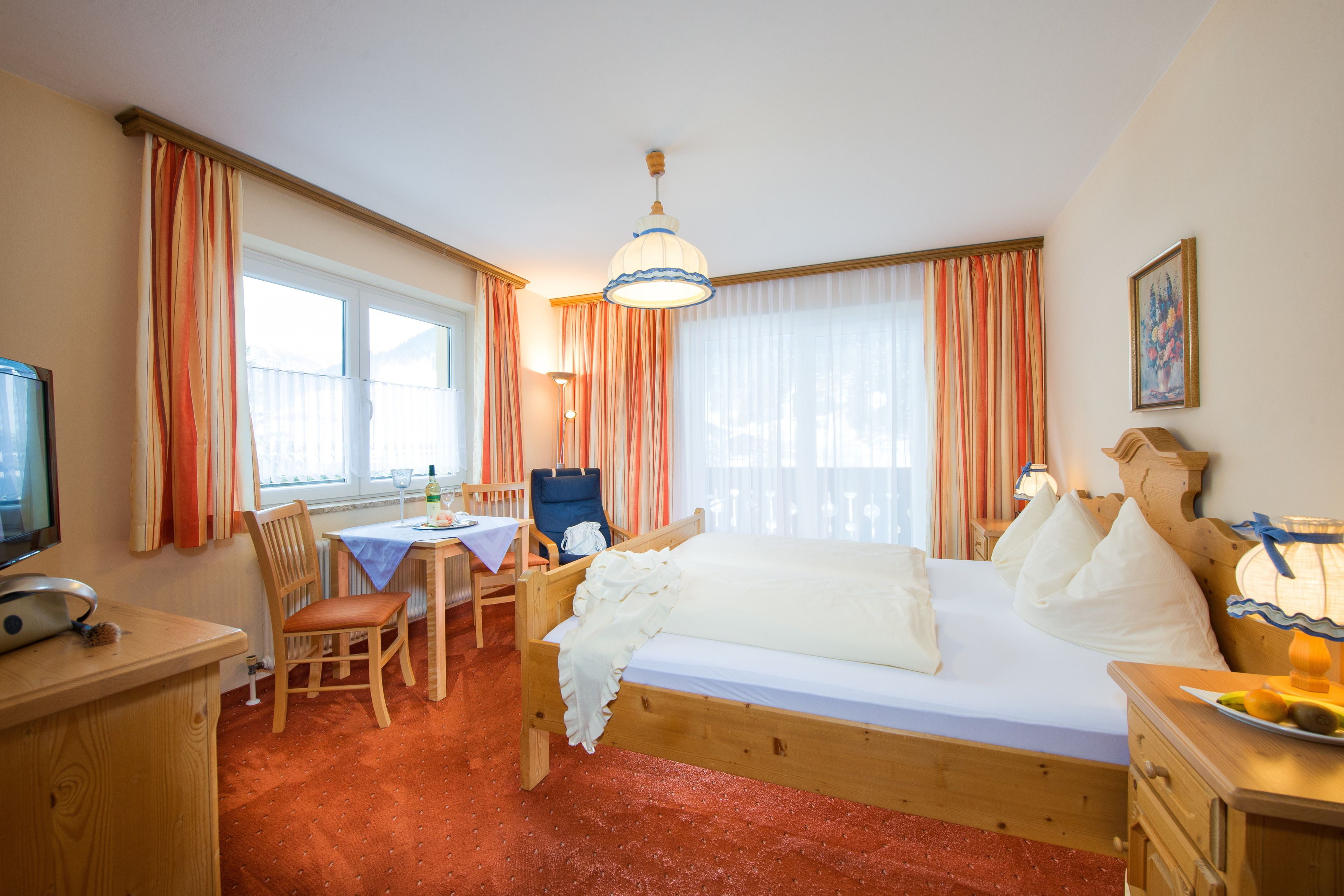A cozy room with a wooden bed, a desk with a chair, a television, and a window with curtains.