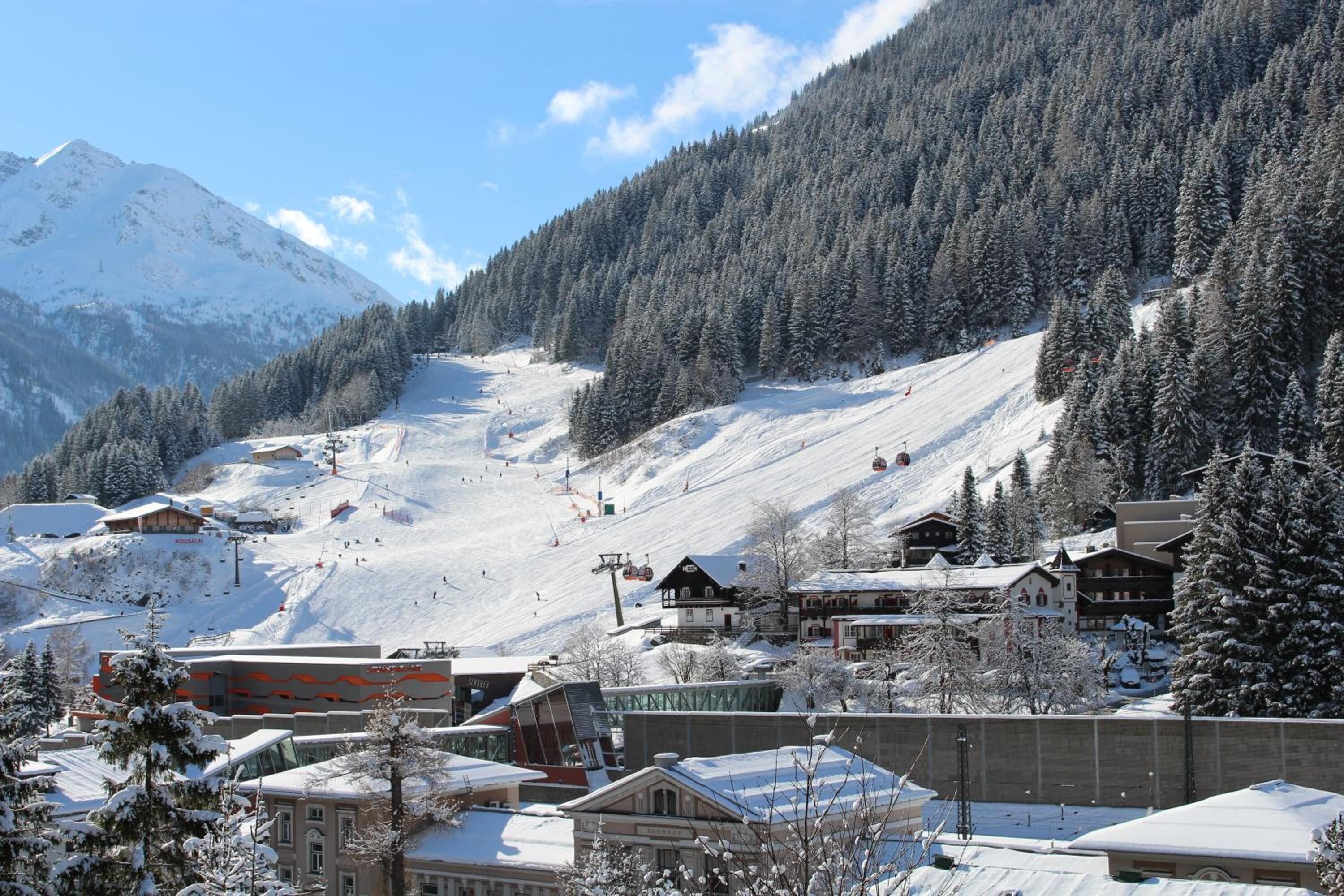 Un pueblo cubierto de nieve en la montaña, con edificios y una pista de esquí.