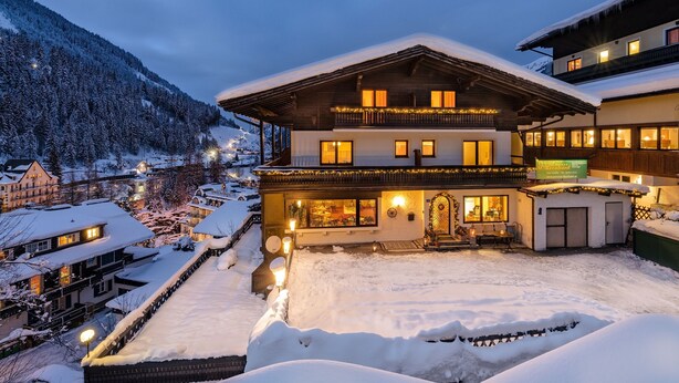 A multi-story hotel with a snow-covered exterior and illuminated windows, surrounded by a snowy landscape and mountains. - Pension St. Leonhard (Bad Gastein)
