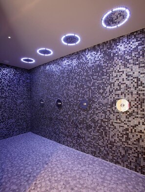 Een badkamer met mozaïektegels op de wanden en het plafond, ronde verlichtingsarmaturen en een gestructureerde vloer.