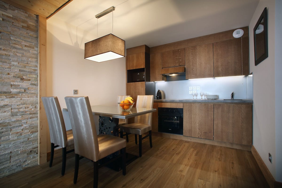 Una cocina moderna con armarios de madera, horno empotrado y comedor con mesa y sillas.