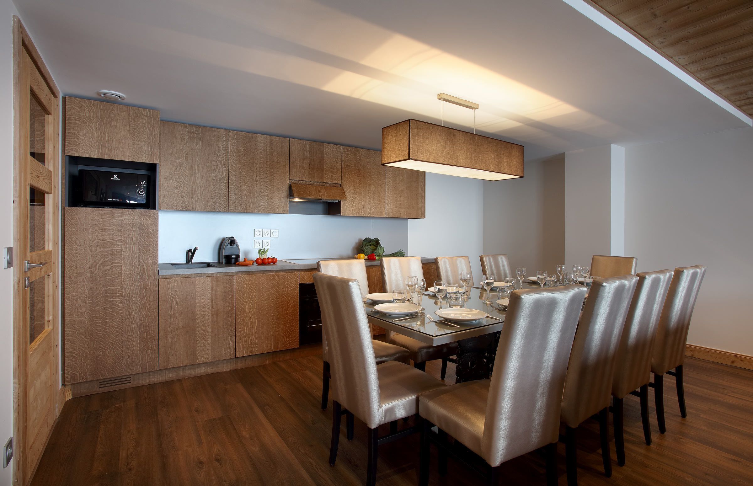 A modern kitchen with wooden cabinets, a microwave, and a dining area with a table set for four.