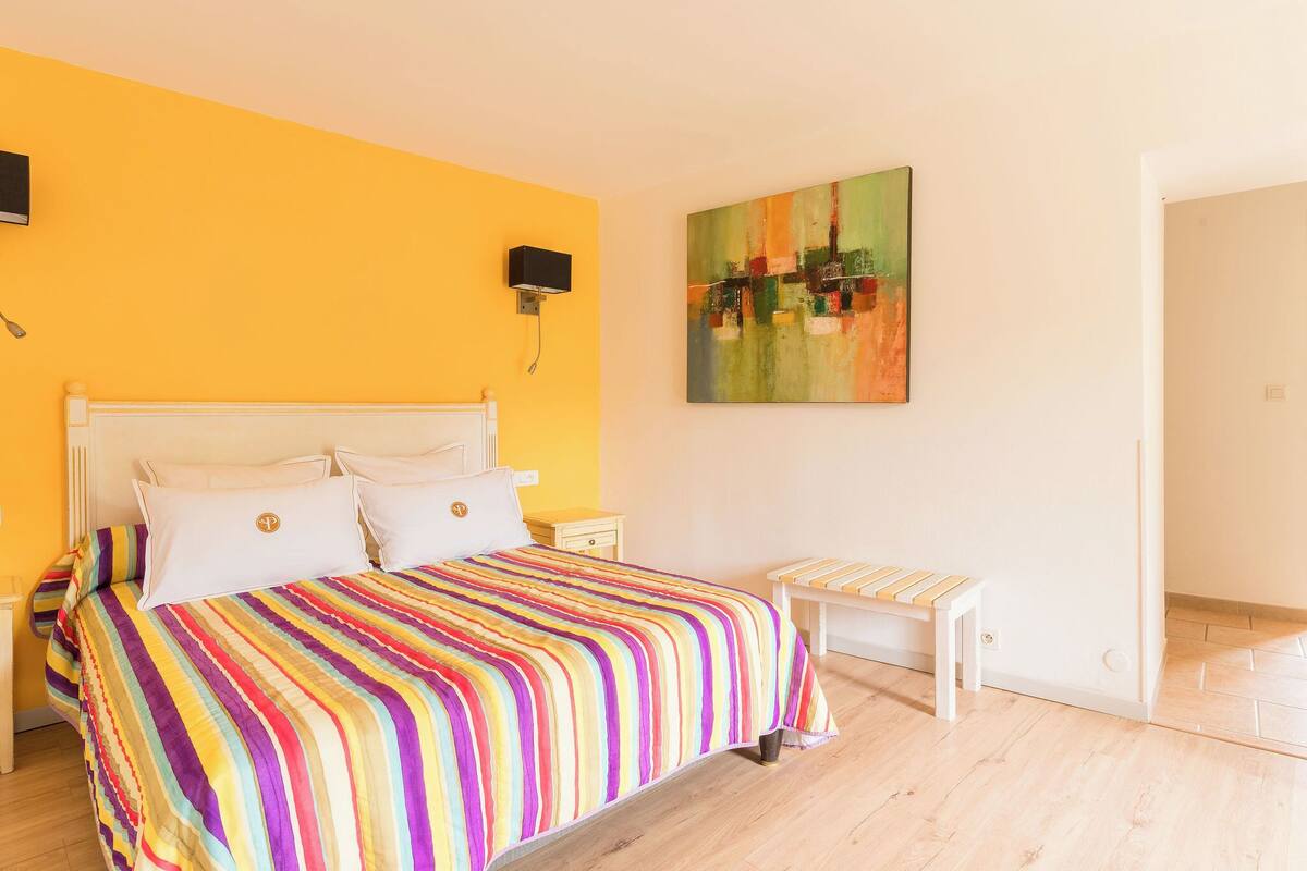 Un dormitorio con cama, mesitas de noche, un banco y un cuadro en la pared.