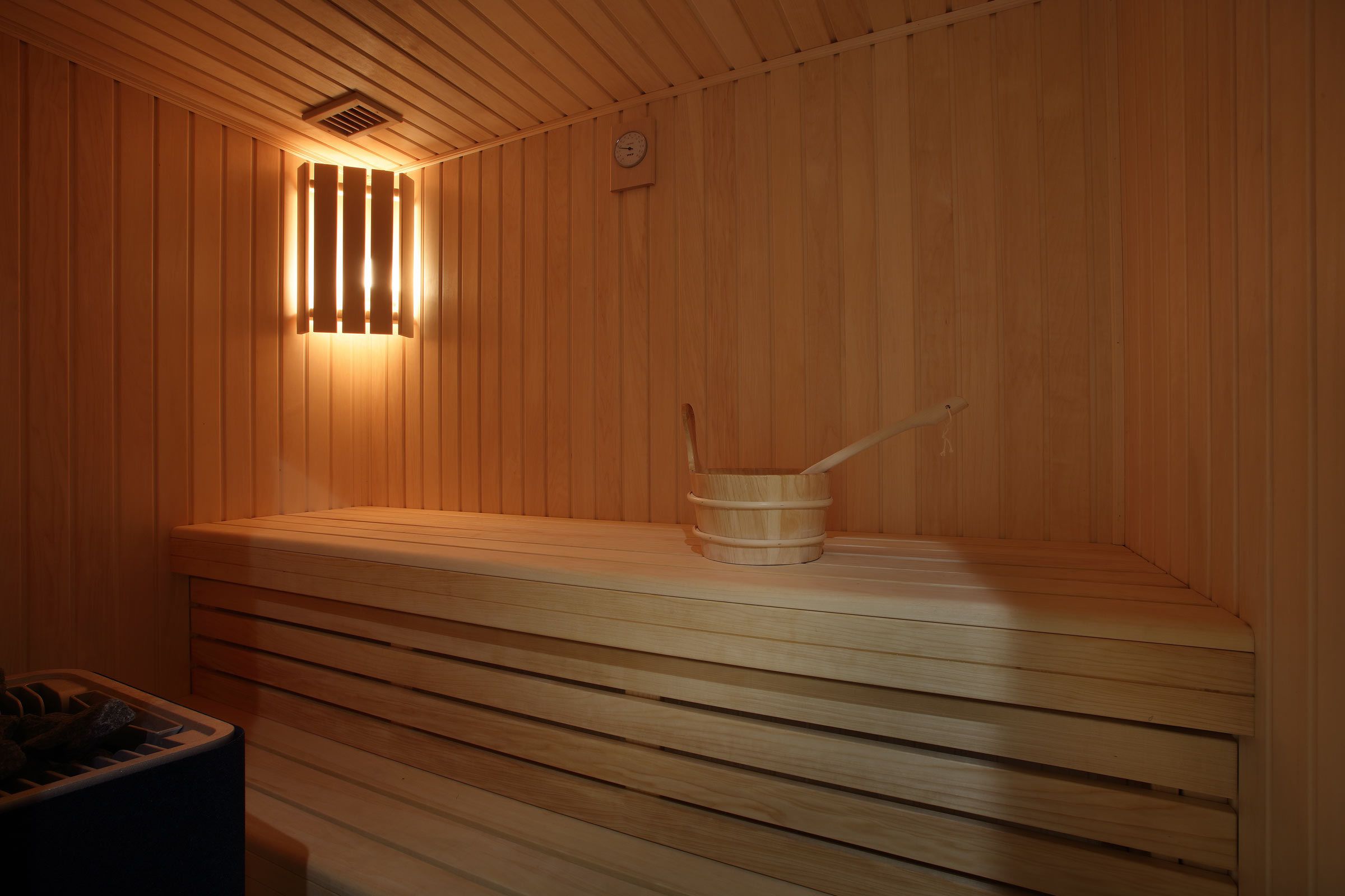 A sauna with wooden walls and benches, a wooden bucket, and a visible clock.