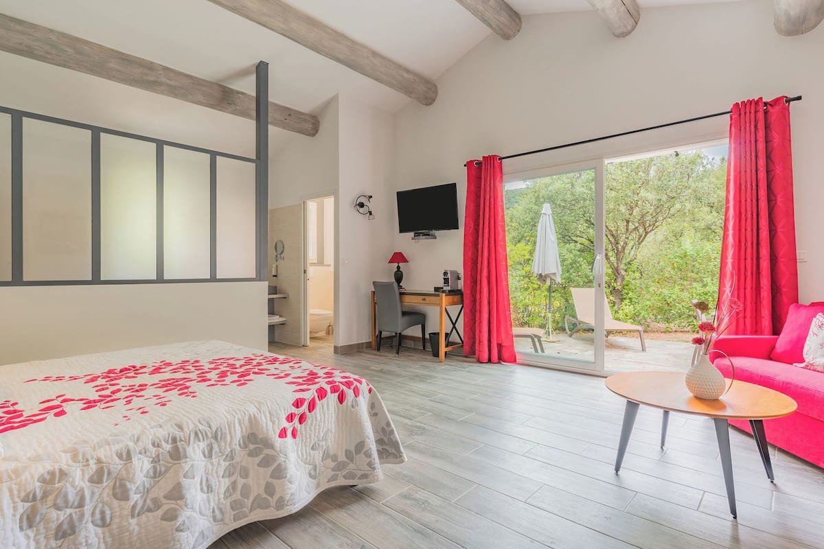 Un dormitorio con cama, escritorio, televisor y puerta corrediza de vidrio a un espacio exterior.