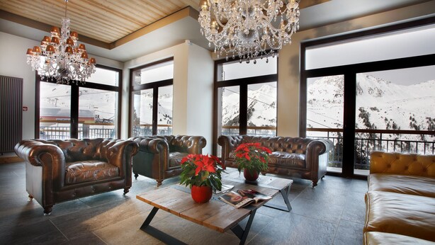 A spacious lobby with leather sofas, a wooden coffee table with red flowers, and large windows offering mountain views. - Chalet des Neiges - LA SOURCE DES ARCS (Bourg-Saint-Maurice)