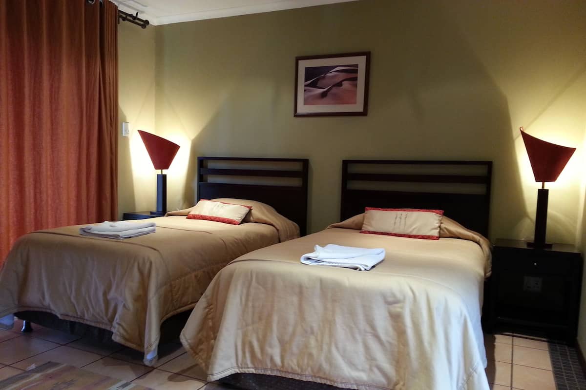 Two single beds with beige bedding, red pillows, and matching nightstands with lamps.