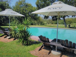 A poolside area with lounge chairs and umbrellas, surrounded by greenery and trees. - The Venue Country Hotel & Spa (Muldersdrift)
