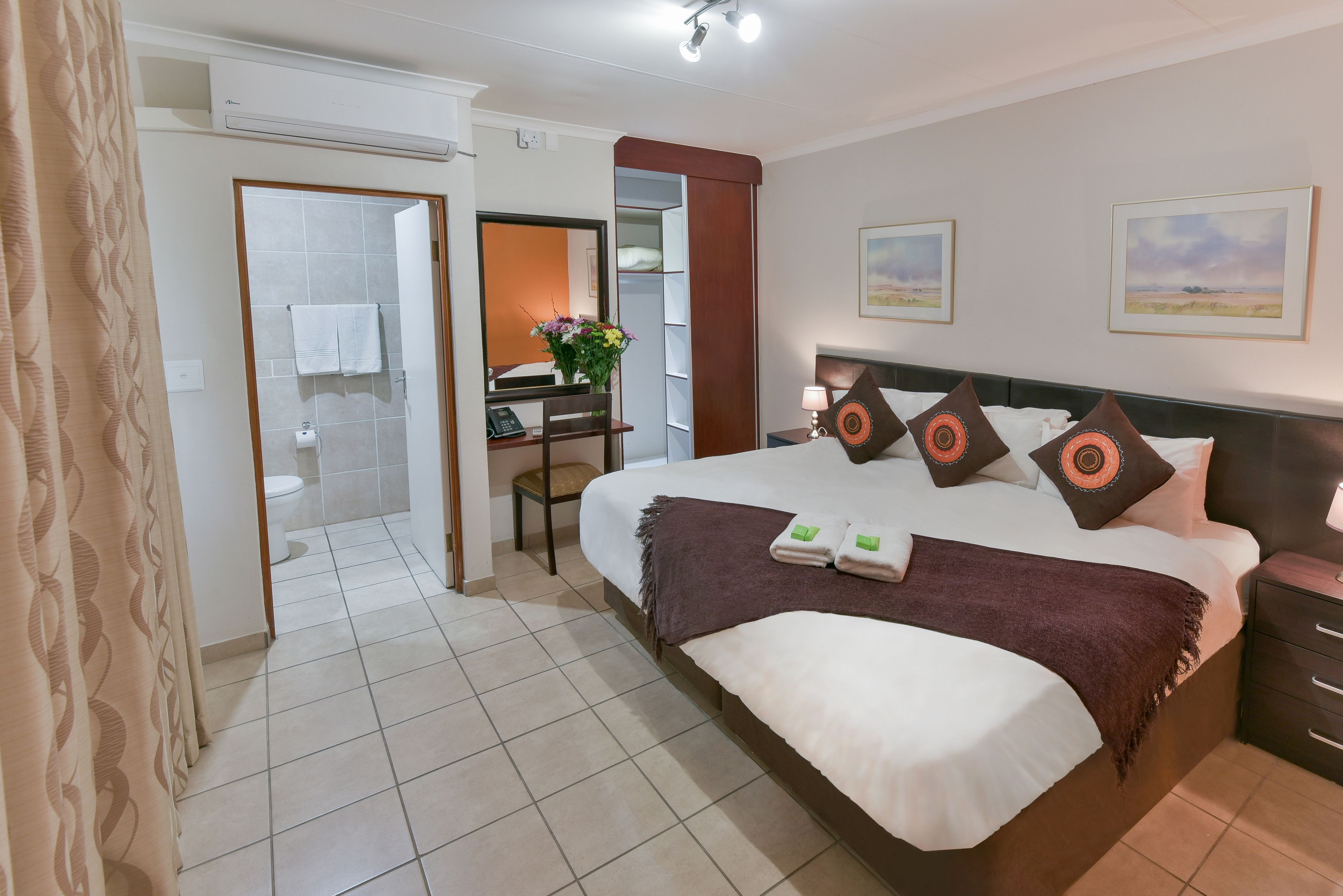 Ein Hotelzimmer mit Bett, Schreibtisch, Stuhl, Nachttisch und einem durchgegangenen Tür einsehbaren Badezimmer.