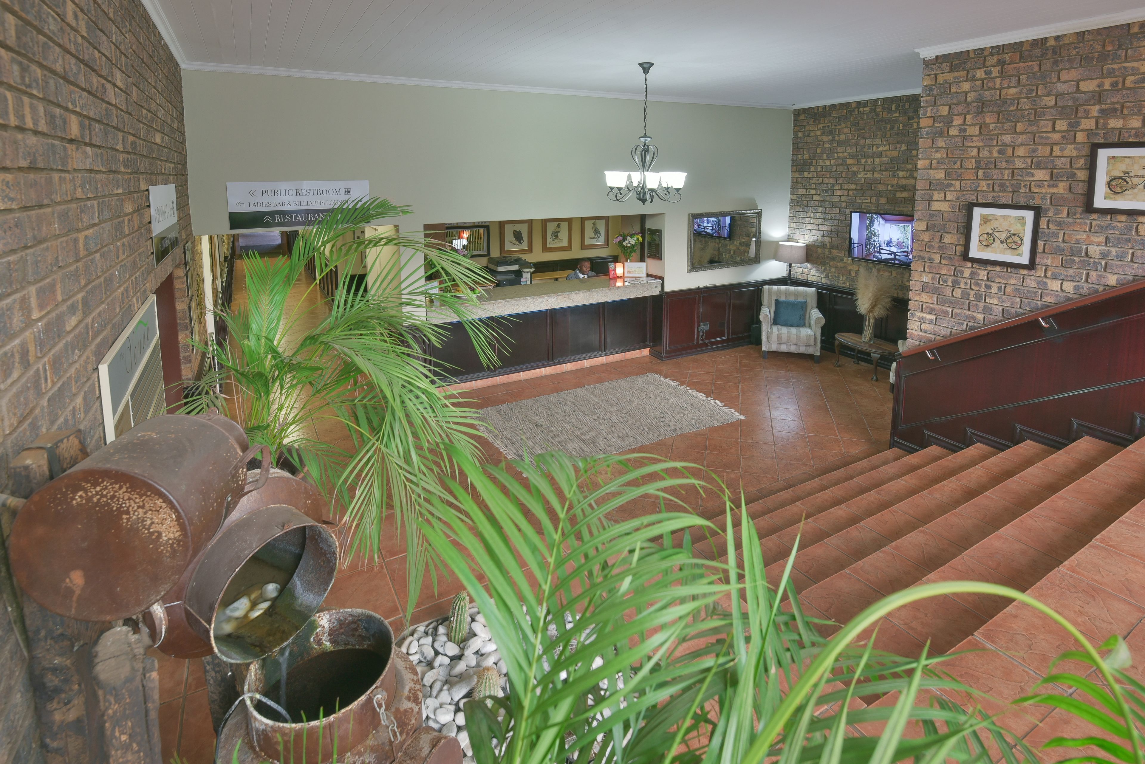 Um lobby com parede de tijolos, balcão de recepção, escada e lustre.