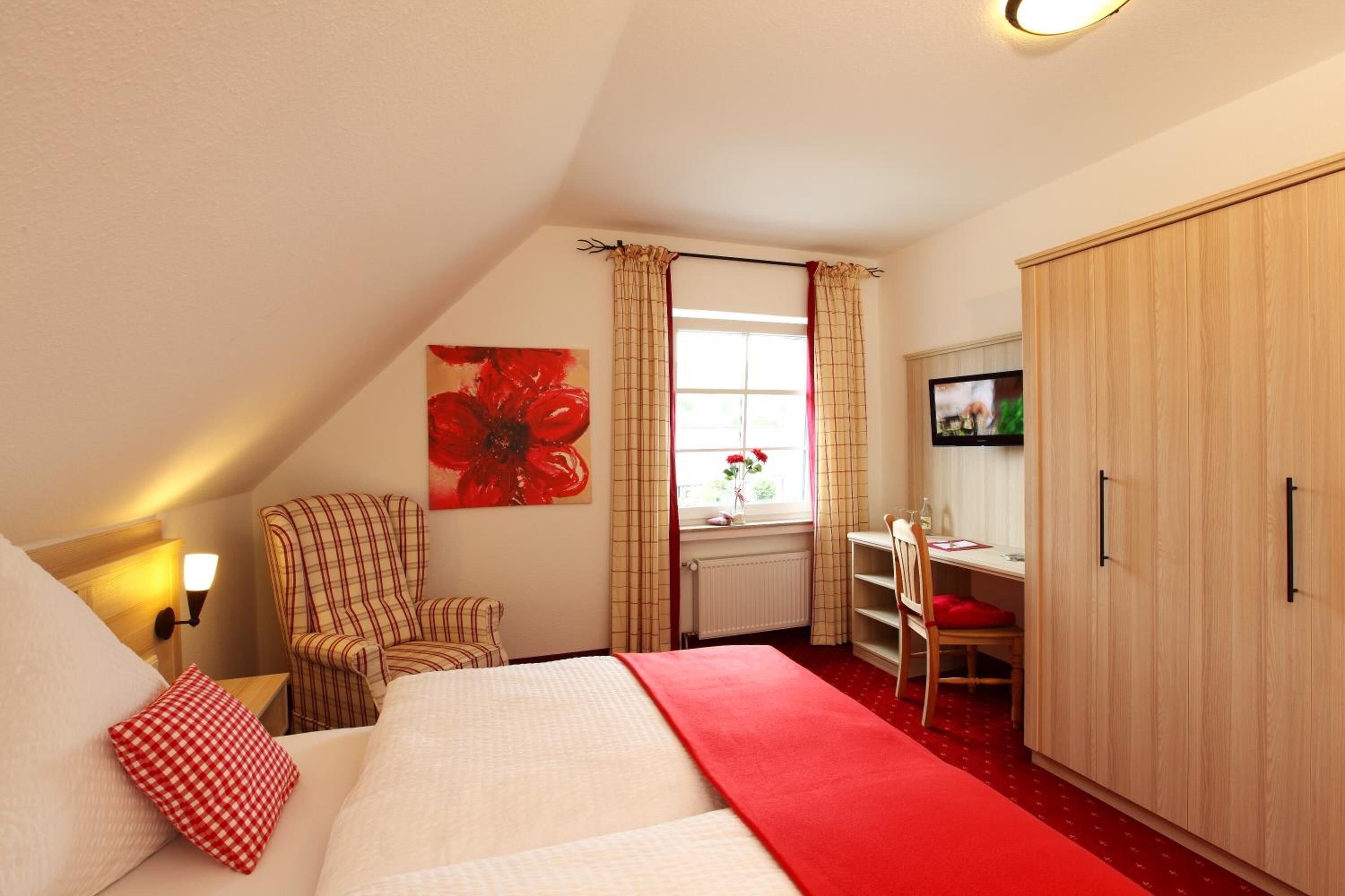A bedroom with a bed, a chair, a desk, a wardrobe, and a window with curtains.