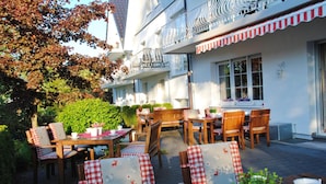 An outdoor patio area with wooden tables and chairs, some with checkered tablecloths. - Hotel Dorfkammer (Olsberg)