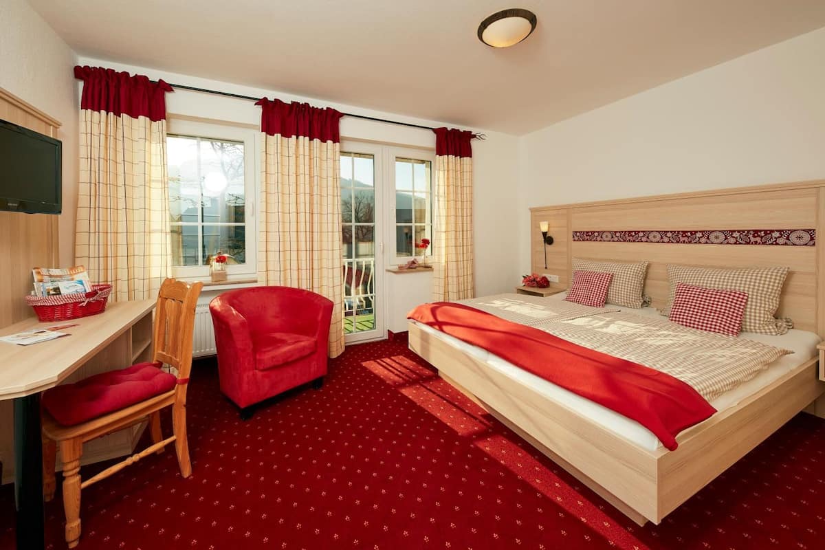 A bedroom with a bed, a desk, a chair, and a window with curtains.
