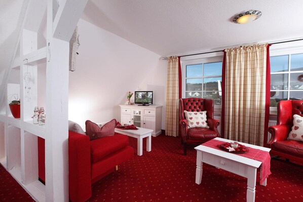 Un salón decorado en rojo con un sofá blanco, un sillón rojo, una mesa de centro blanca y un televisor sobre un mueble blanco.