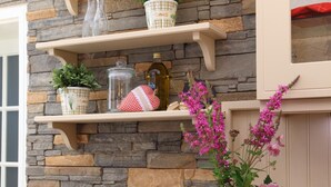 A stone wall with shelves holding potted plants, a vase with flowers, and decorative items. - Hotel Dorfkammer (Olsberg)