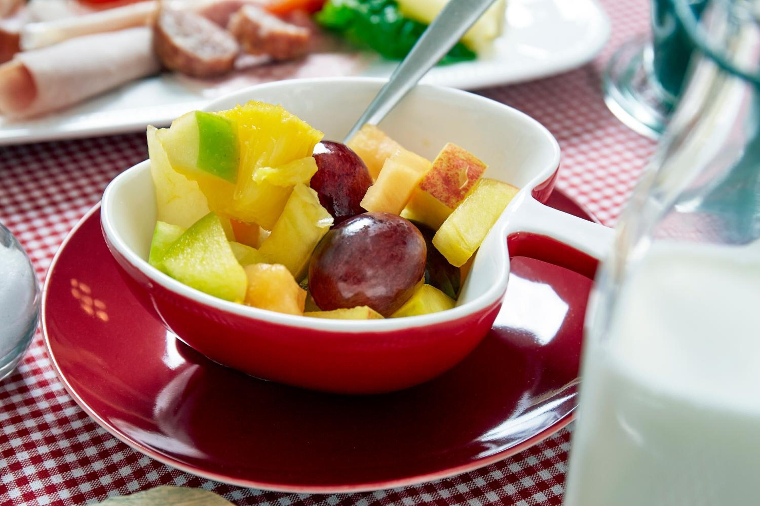 A bowl of fruit salad with a spoon, placed on a red plate.