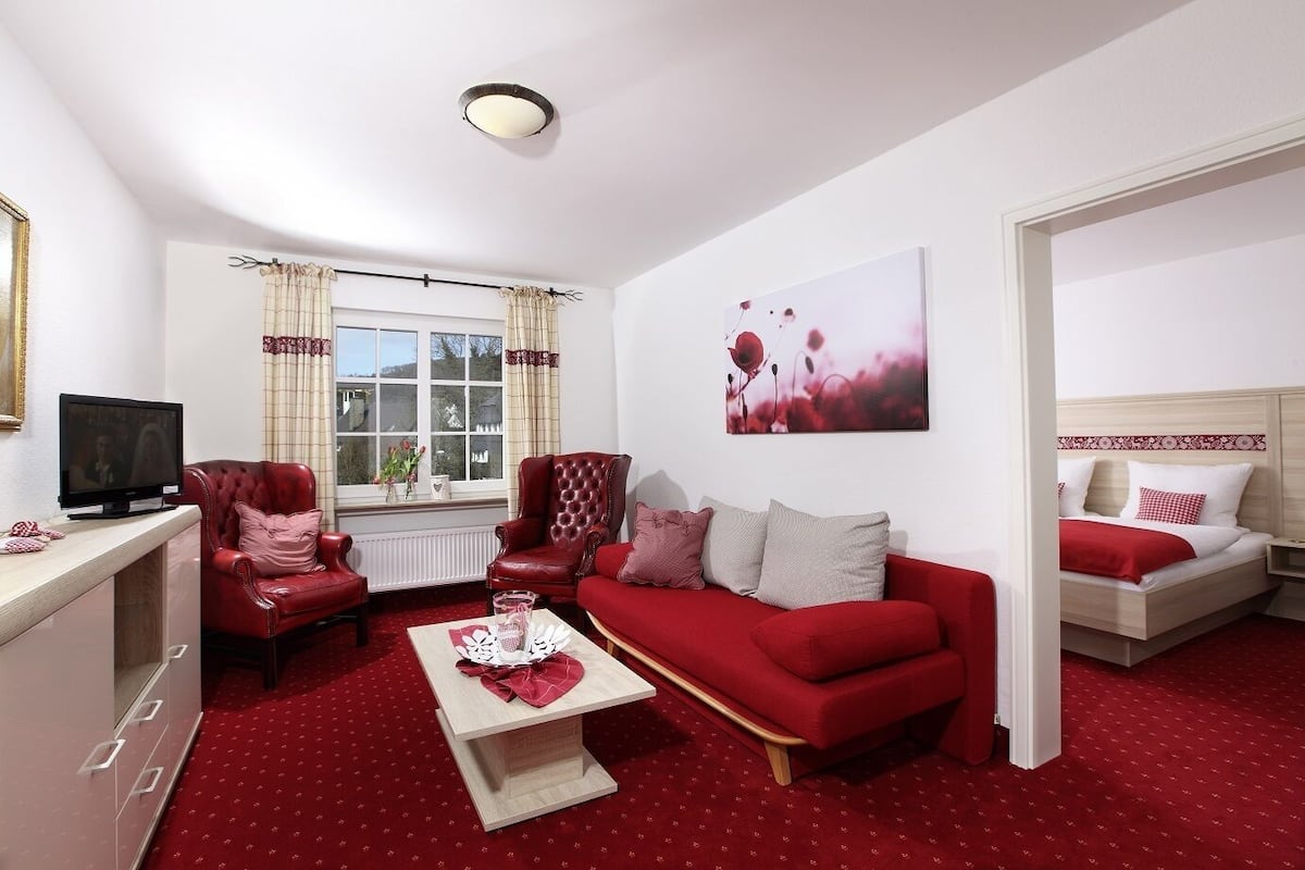 A living room with a red sofa, a red armchair, a TV, and a painting on the wall.
