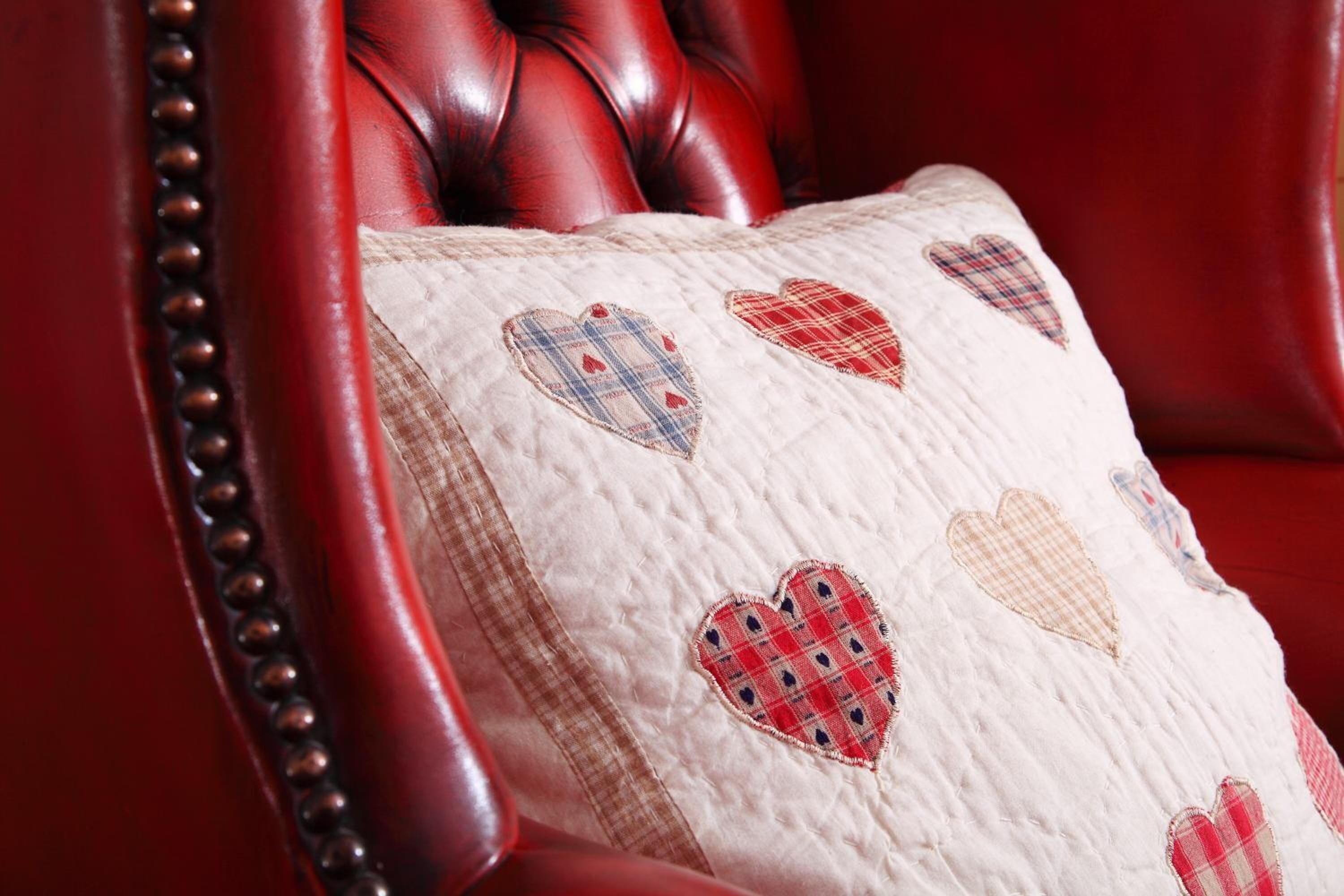 A red leather chair with a quilted pillow featuring heart patterns.