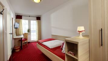 A hotel room with a bed, a desk, a chair, a lamp, and a wardrobe.