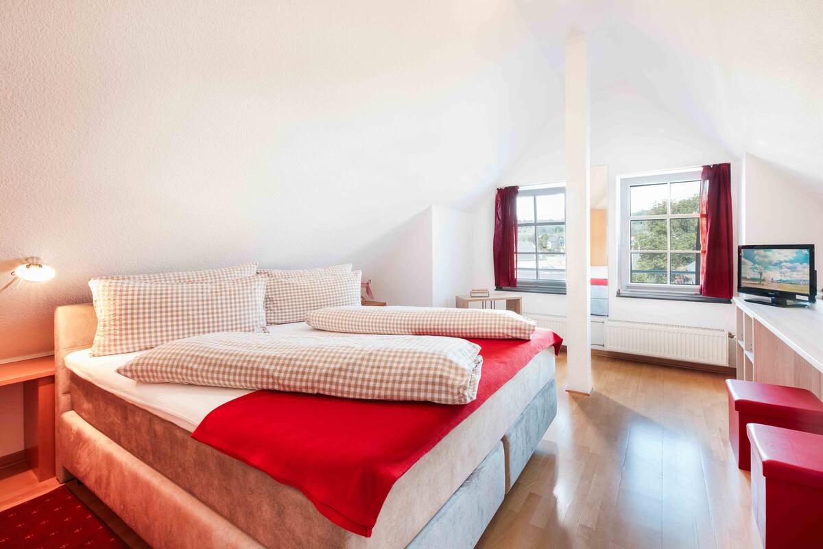 A bedroom with a bed, a desk, a chair, and a TV.