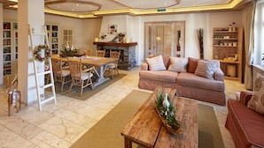 A spacious living area with a fireplace, a sofa, a dining table, and a bookshelf. - Hotel Dorfkammer (Olsberg)