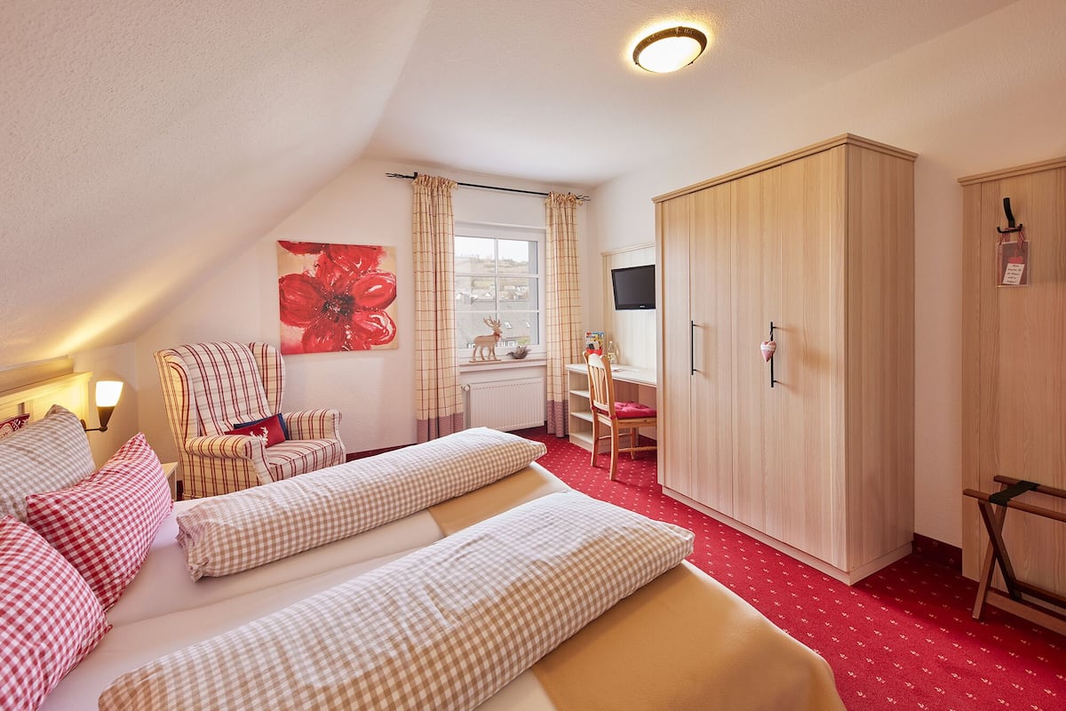 A bedroom with a bed, two chairs, a desk, a wardrobe, and a window with curtains.