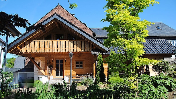 A wooden house with a sloped roof, a porch, and a garden with various plants. - Hotel Dorfkammer (Olsberg)